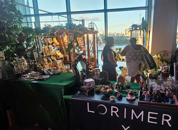 Table with various items and a sign reading 'Lorimer' in an indoor setting with large windows.