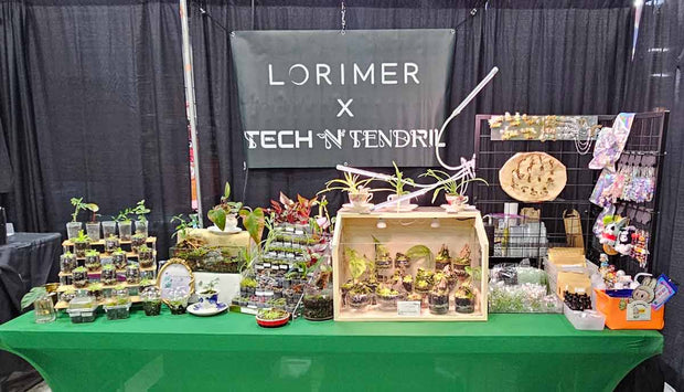 Table with various items and a backdrop displaying 'Lorimer x Tech N' Tendril at an event.